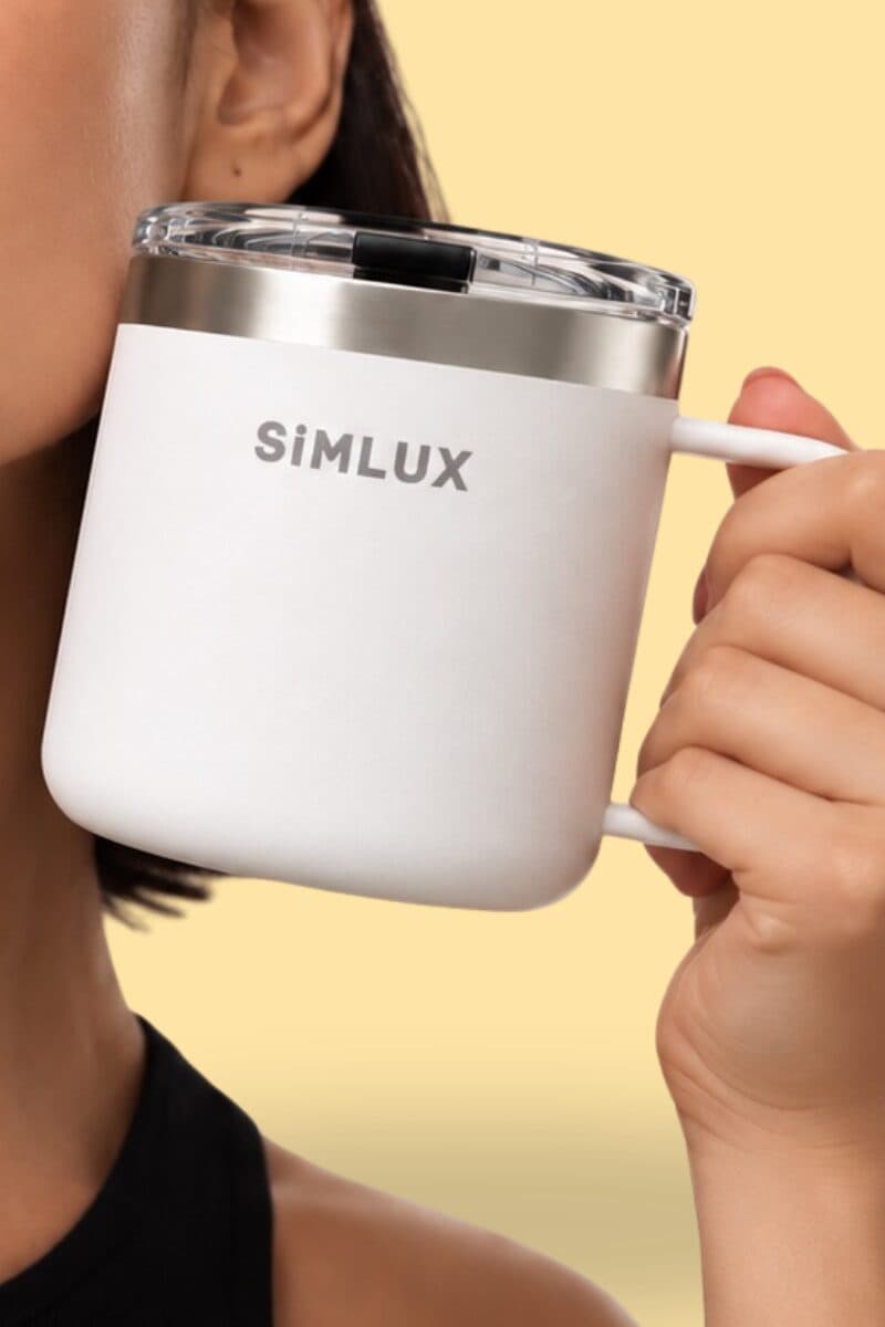 Model holding a White SiMLUX Mug against her cheek on a yellow backdrop